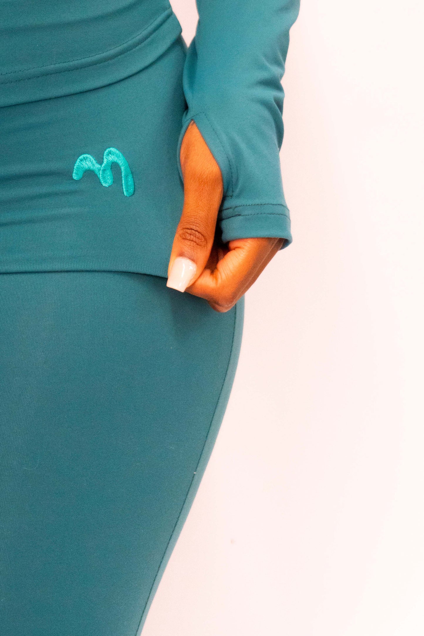 Woman in a teal green fold over legging with the brand logo on the hip.